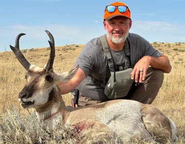 A hunter wearing a dark gray shirt and orange hat kneels beside a trophy pronghorn antelope, a successful hunt in Wyoming captured during their SNS guided experience.